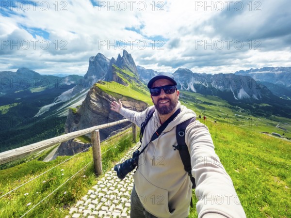 Photographer with backpack and camera taking a selfie portrait with outstretched arm in the seceda mountain range in the italian dolomites, during summer