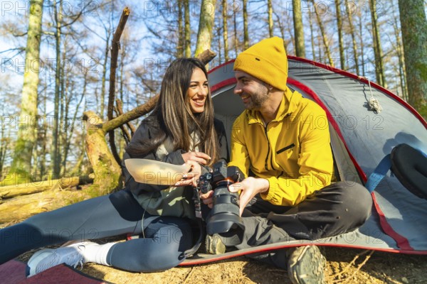 Couple of photographers camping and having a meal while reviewing photos they have taken in the forest