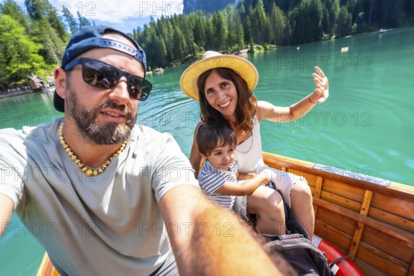 Happy family with a child taking a selfie while enjoying a boat trip on the beautiful lake braies in the dolomites, italy, during summer