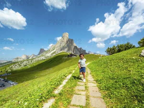 Happy child running on a path at giau pass in the italian dolomites with a mountain peak and blue sky in the background