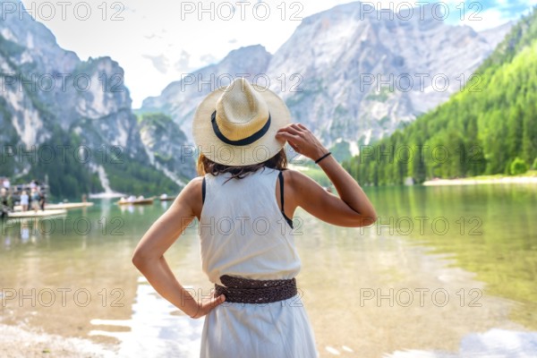 Woman wearing straw hat, enjoying the amazing view of lake braies in the dolomites mountains during summer