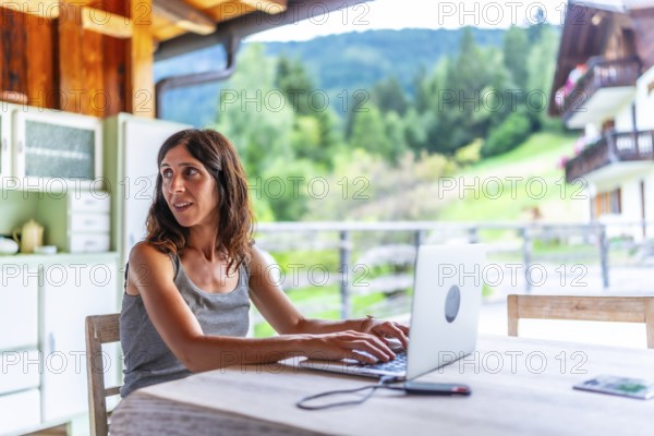 Freelancer woman working remotely on vacation with a laptop in a mountain chalet, enjoying the view of the dolomites