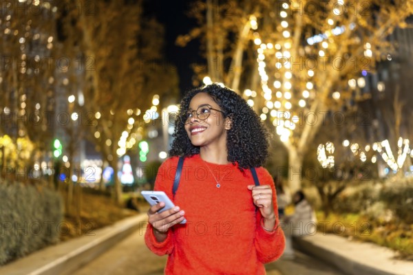 Smiling student walking in a decorated city using her smartphone during christmas holidays