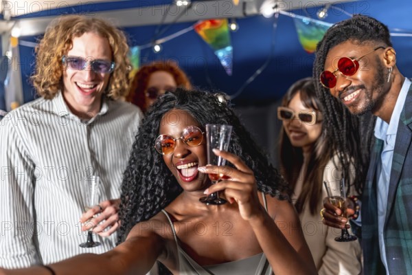 Multi-ethnic chic friends enjoying party at night and taking selfie together while raising champagne glasses