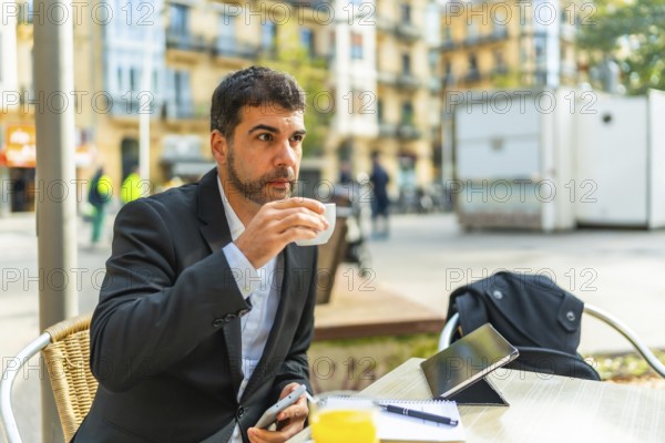 Businessman enjoying morning coffee while working with smartphone and digital tablet in an outdoor cafeteria