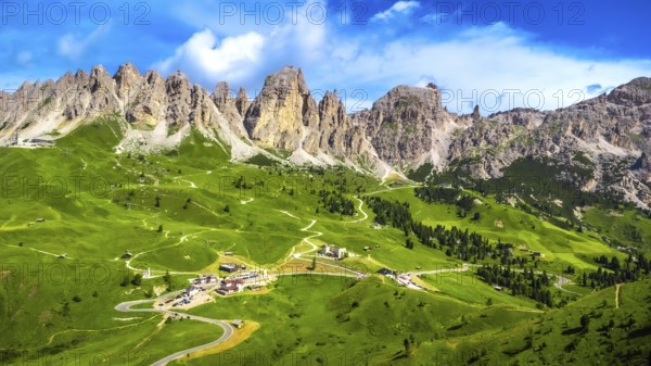 Stunning aerial view of the picturesque gardena pass winding through lush green valleys, embraced by the majestic dolomites peaks under a vibrant blue sky