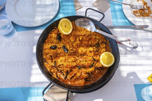 Steaming seafood paella featuring mussels, shrimps, clams, and lemon wedges served in a traditional pan on a vibrant blue table