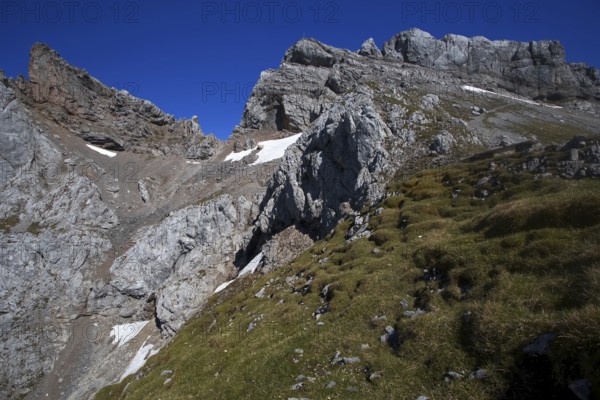 Steep mountain face with scattered snow fields and green grassy areas under a clear sky, Karwendel, Mittenwald, Bavaria, Germany, Europe