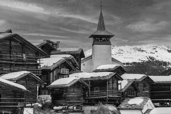 Old wooden houses with snow-covered roofs and the Saint Theodule church in the historic village centre, black and white photograph, Grimentz, Val d'Anniviers, Valais Alps, Canton Valais, Switzerland, Europe