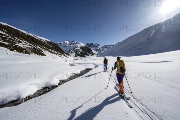 Two ski tourers in the snow by a mountain stream in the Funtauna Valley, Graubünden Haute Route, Albula Alps, Rhaetian Alps, Graubünden, Switzerland, Europe