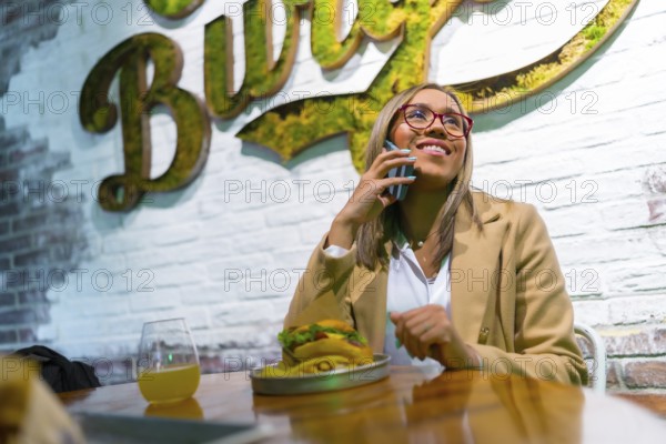 Stylish latin beauty blonde woman talking to the phone eating burger at restaurant