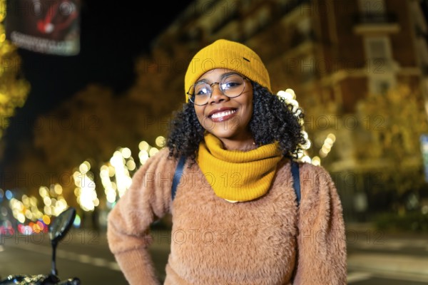 Portrait of a young woman wearing winter clothes and smiling in a city street decorated with christmas lights
