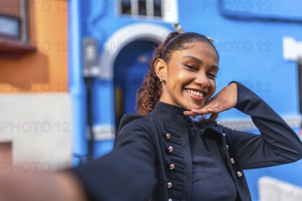 Beauty flirty african american woman gesturing hand down chin smiling while taking a selfie in a colorful street