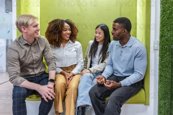 Four smiling colleagues enjoying a relaxed conversation in a modern, green coworking office, demonstrating teamwork and collaboration