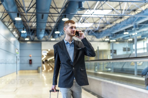 Businessman pulling suitcase and making phone call while walking through airport terminal