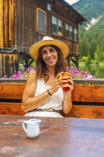 Woman wearing a straw hat enjoying a hot beverage in a mountain chalet by the lake in the italian dolomites