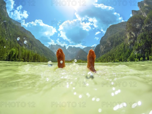 Feet of a tourist floating in the turquoise water of lago di landro, surrounded by the breathtaking panorama of the dolomites on a sunny summer day