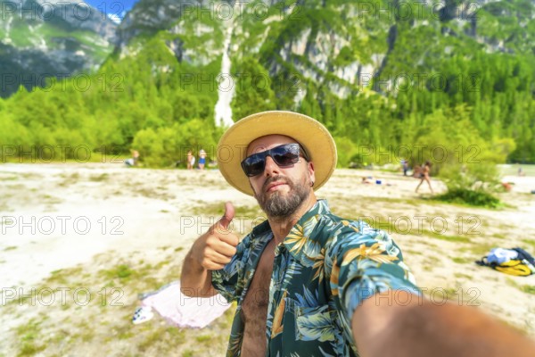 Happy tourist showing thumbs up while taking a selfie at lago di landro, also known as durrensee lake, with a waterfall in the background in the dolomites