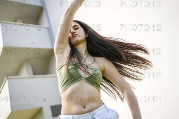 Low angle view motion photo of a caucasian young woman dancing energetically raising arm in the city
