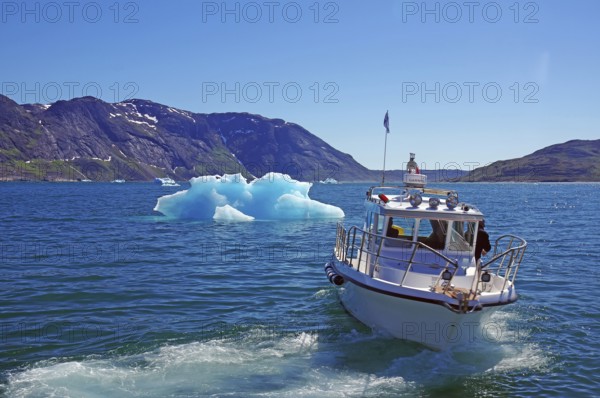 Boat sailing on a blue sea with iceberg and mountains in the background under a sunny sky, small passenger ferry between settlements, Igaliku, North America, Greenland, Denmark, North America