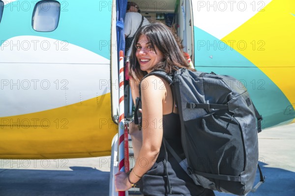 Female tourist exiting airplane after landing in philippines airport, carrying backpack and smiling