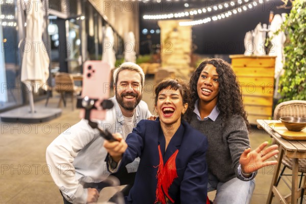 Caucasian adult female vlogger laughing with diverse friends celebrating night party and recording a new video online for the audience