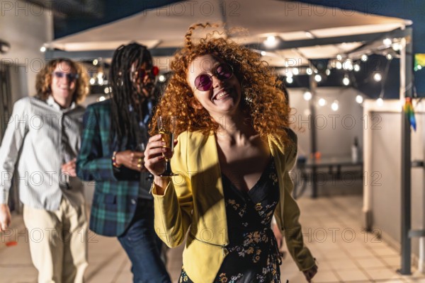 Happy redhead woman dancing passionately at night terrace party with multiracial friends