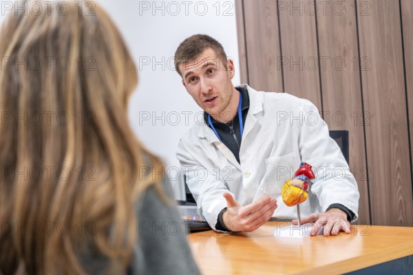 Doctor cardiologist using a model of a heart to explain surgery to a female patient