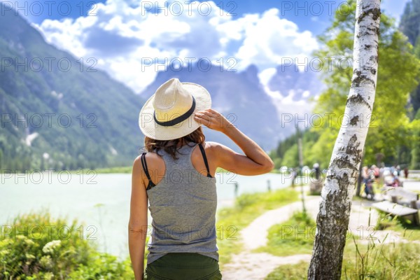 Woman wearing straw hat enjoying the view of the beautiful lago di landro with the dolomites in the background on a summer day, italy