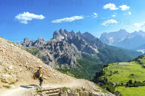 Female tourist hiking on a mountain trail with breathtaking views of the tre cime di lavaredo peaks in the italian dolomites on a sunny summer day