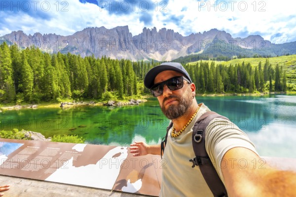 Tourist taking a selfie at lake carezza, with the stunning latemar massif and picturesque dolomites in the background