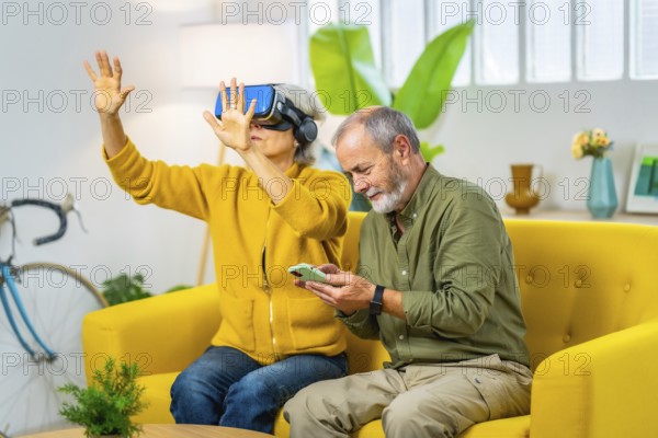 Senior woman using virtual reality googles next to her husband sitting on the sofa using mobile phone