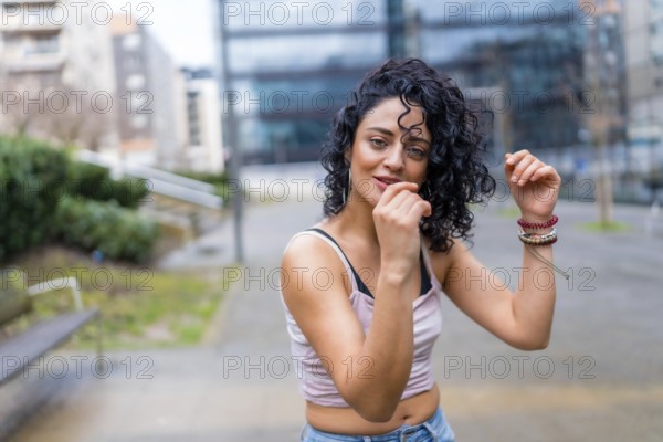 Stylish young woman with curly hair enjoying dancing outdoors, showcasing urban lifestyle and carefree movement