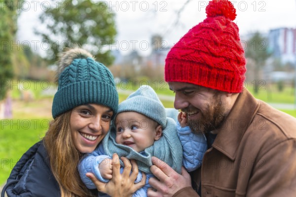 Smiling parents holding their baby, enjoying a joyful winter day together at the park, creating cherished memories in the crisp air