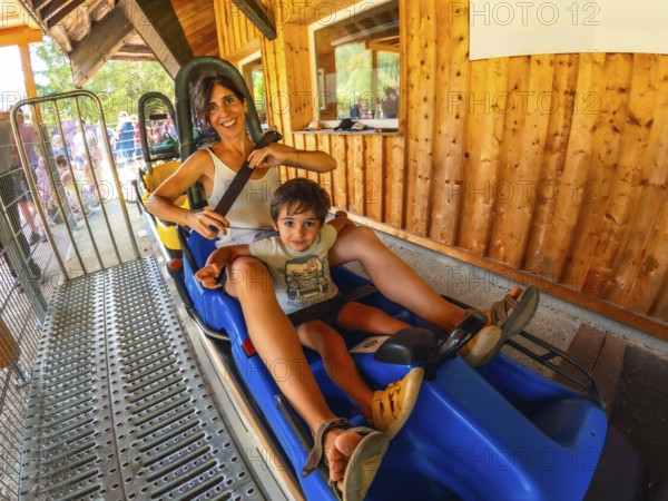 A woman and a child are riding a roller coaster. The woman is holding the child's hand