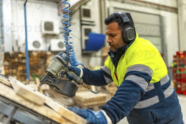 Side view of a caucasian adult man manual worker using compressed air gun to arrange a pallet in a recycling plant