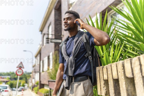 African young businessman talking to the mobile in the city standing holding laptop in a residential area