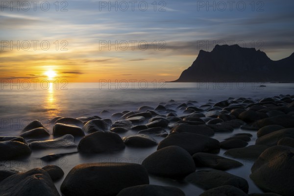Seascape on the beach at Uttakleiv (Utakleiv), in the foreground round stones in the sea. In the background the mountain Hogskolmen. At night at the time of the midnight sun. The sun is low in the sky. Early summer. Long exposure. Uttakleiv, Vestvagoya, Lofoten, Norway, Europe