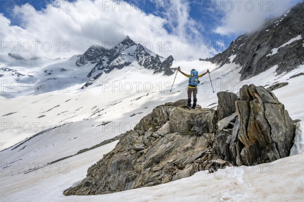 Mountaineer on a rock between snow, raises her arms triumphantly, descending from the summit of Schönbichler Horn, view of snow-covered and glaciated mountain landscape with summit Großer Möseler, Berliner Höhenweg, Zillertal Alps, Tyrol, Austria, Europe