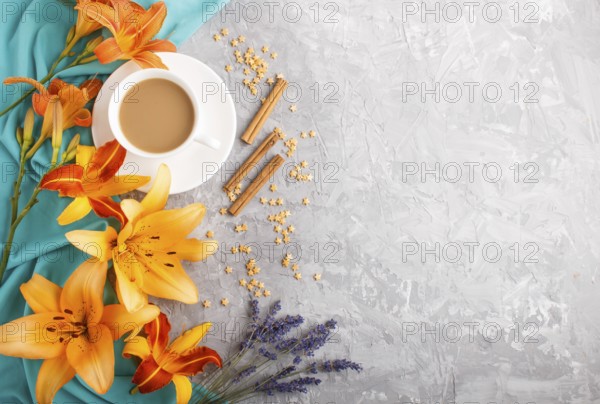 Orange day-lily and lavender flowers and a cup of coffee on a gray concrete background, with blue textile. Morninig, spring, fashion composition. Flat lay, top view, copy space