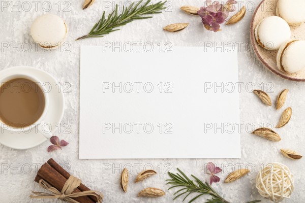 White paper sheet mockup with cup of coffee, almonds and macaroons on gray concrete background. Blank, business card, top view, flat lay, still life