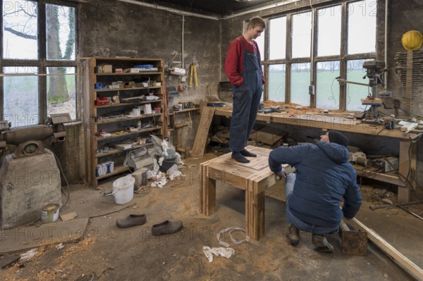 Young man tests the durability of his Tiasch in the workshop, his father looks on, Mecklenburg-Vorpommern, Germany, Europe