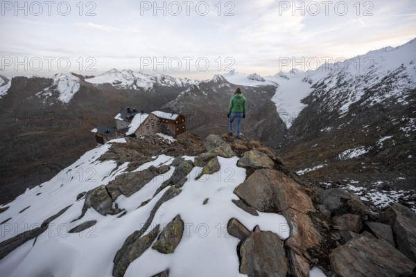 Mountaineer looking at mountain panorama and glacier, mountain hut Ramolhaus in autumn with snow, at sunset, view of Gurgler Ferner with summit Hochwilde and Falschungsspitze, Ötztal Alps, Tyrol, Austria, Europe