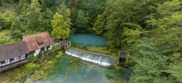Blautopf Blaubeuren with industrial monument Hammerschmiede, source of the little river Blau in a landscape with forest. Karst spring, geotope and geopoint of the UNESCO Swabian Alb Geopark, tourist attraction. The popular excursion destination is now being thoroughly renovated and will therefore be closed to visitors until the end of 2028. Drone photo. Blaubeuren, Baden-Württemberg, Germany, Europe