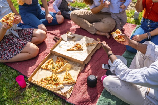 Group of friends and families having fun, eating pizza and relaxing during a picnic in a park