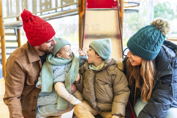 Happy family dressed in warm winter clothing enjoying playful moments together on a playground slide, creating joyful memories outdoors