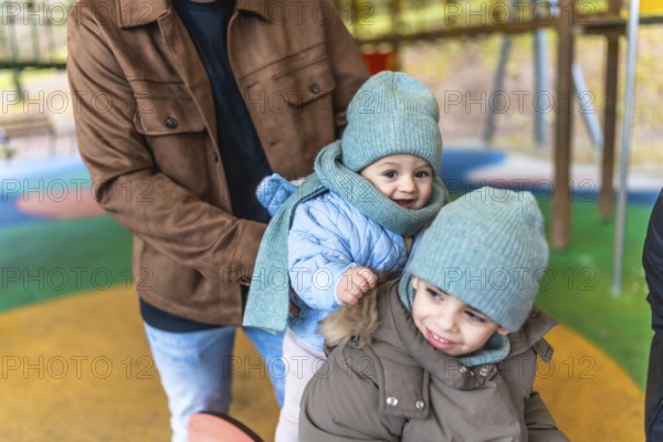 Father holding two joyful children in colorful winter clothes while enjoying playful moments at an indoor playground, creating cherished memories