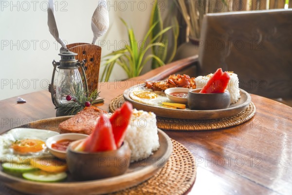 Two plates of filipino breakfast featuring tocino, fried rice, fried egg, watermelon, cucumber, and tomato on a wooden table in siargao island, philippines