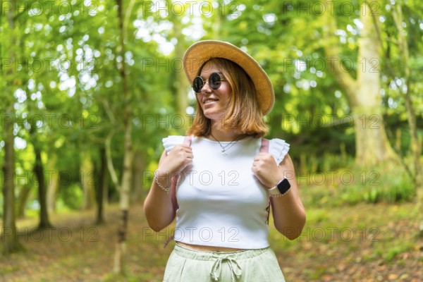 Beauty female caucasian tourist wearing sun hat and sunglasses walking along a green forest in spring