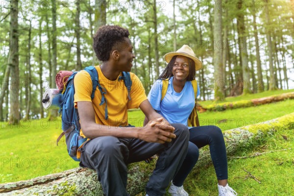Two male and female african friends resting and chatting during a hiking in the forest